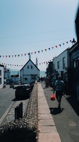 Broad Street in Lyme Regis with red, white, and blue bunting strung across the buildings and the sea visible at the far end.
