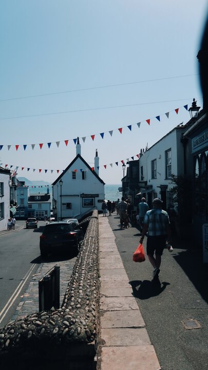 Broad Street in Lyme Regis with red, white, and blue bunting strung across the buildings and the sea visible at the far end.