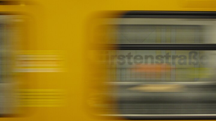 U‑Bahnhof Kurfürstenstraße platform sign seen through a train window as a yellow U‑Bahn blurs past. Photo taken in February 2024.