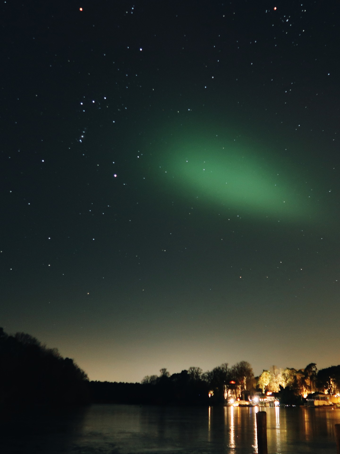 A green aurora streaks across the dark night sky over Kleiner Wannsee.